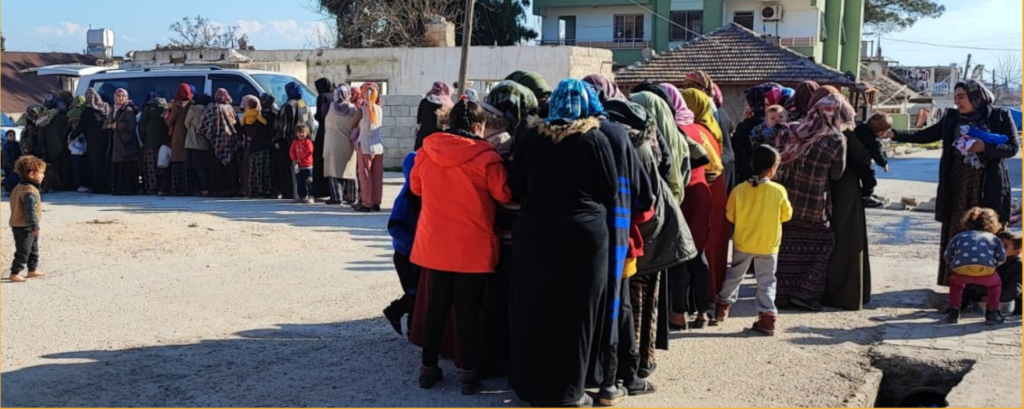 Women and children waiting in line for food, blankets, and hygiene products.